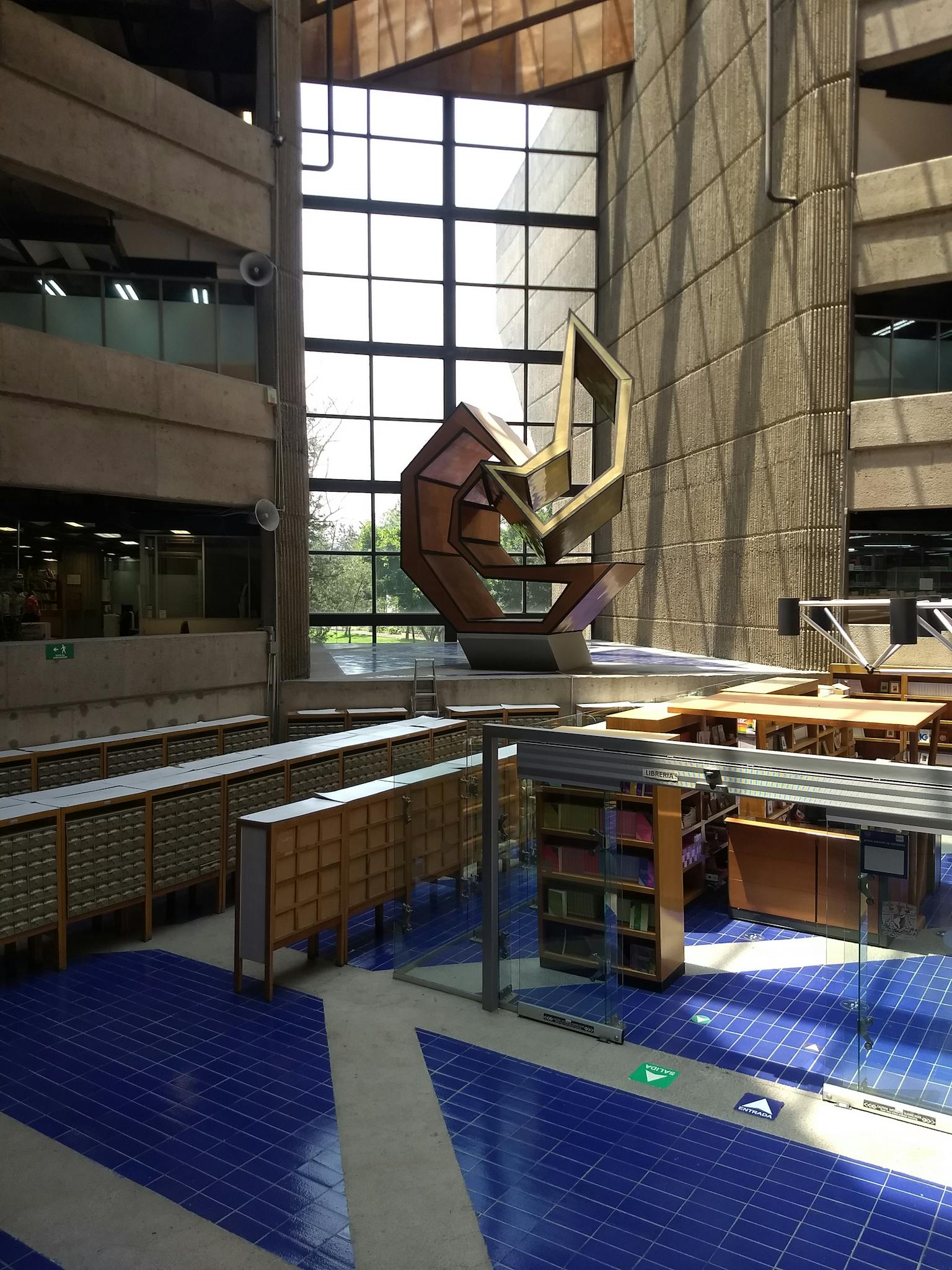 A spacious modern library interior featuring an abstract sculpture and blue tiled floors.