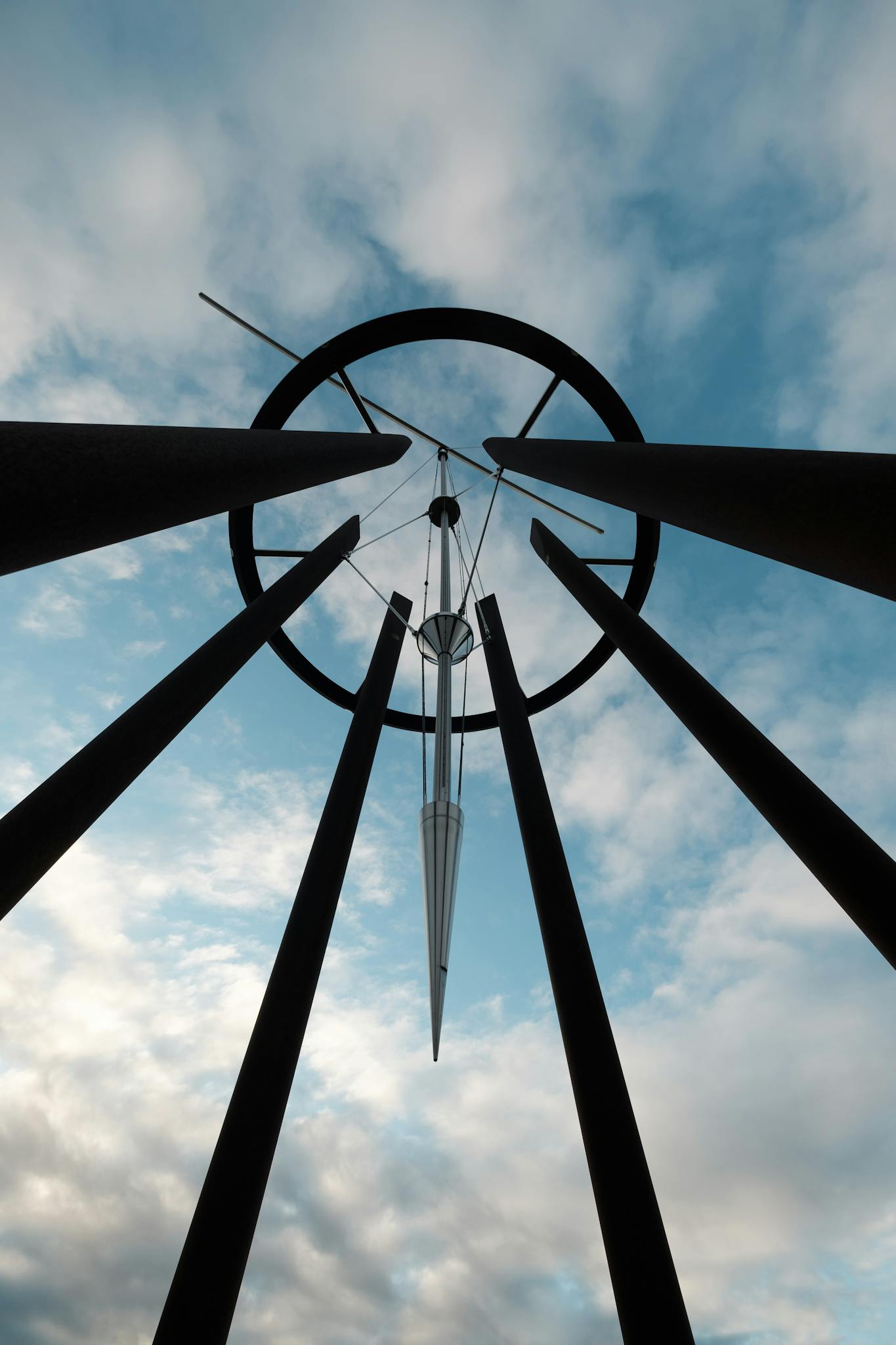 A striking modern sculpture with metal beams reaching towards a blue, cloudy sky.