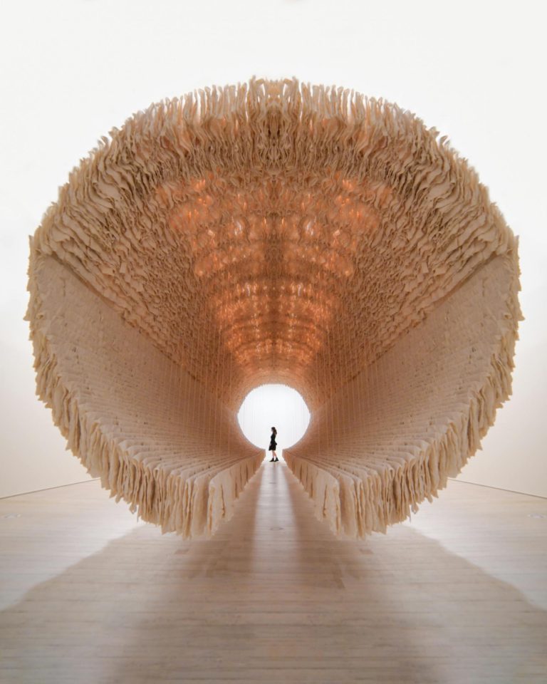A visitor stands inside a large, circular, abstract art installation at a gallery.