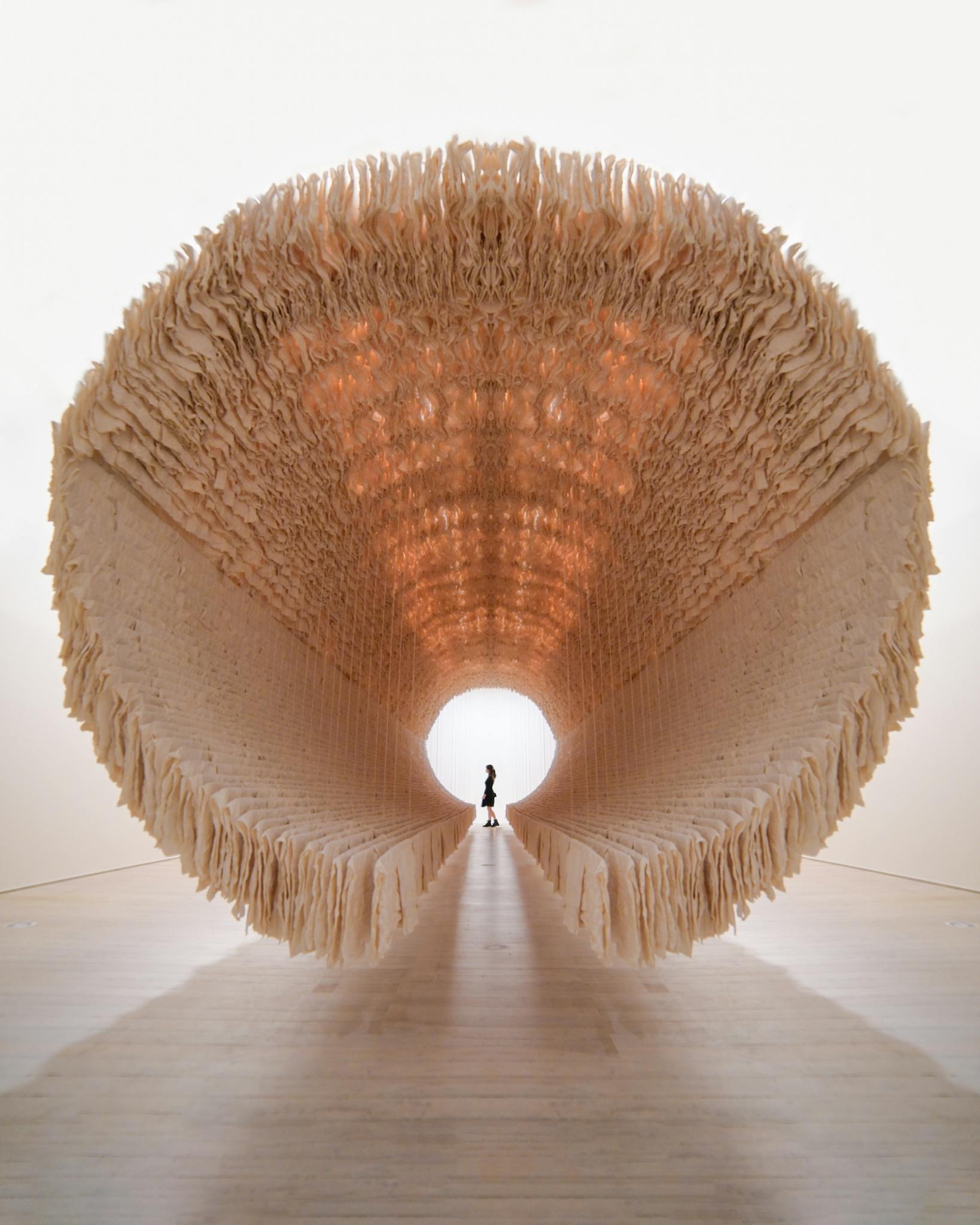 A visitor stands inside a large, circular, abstract art installation at a gallery.